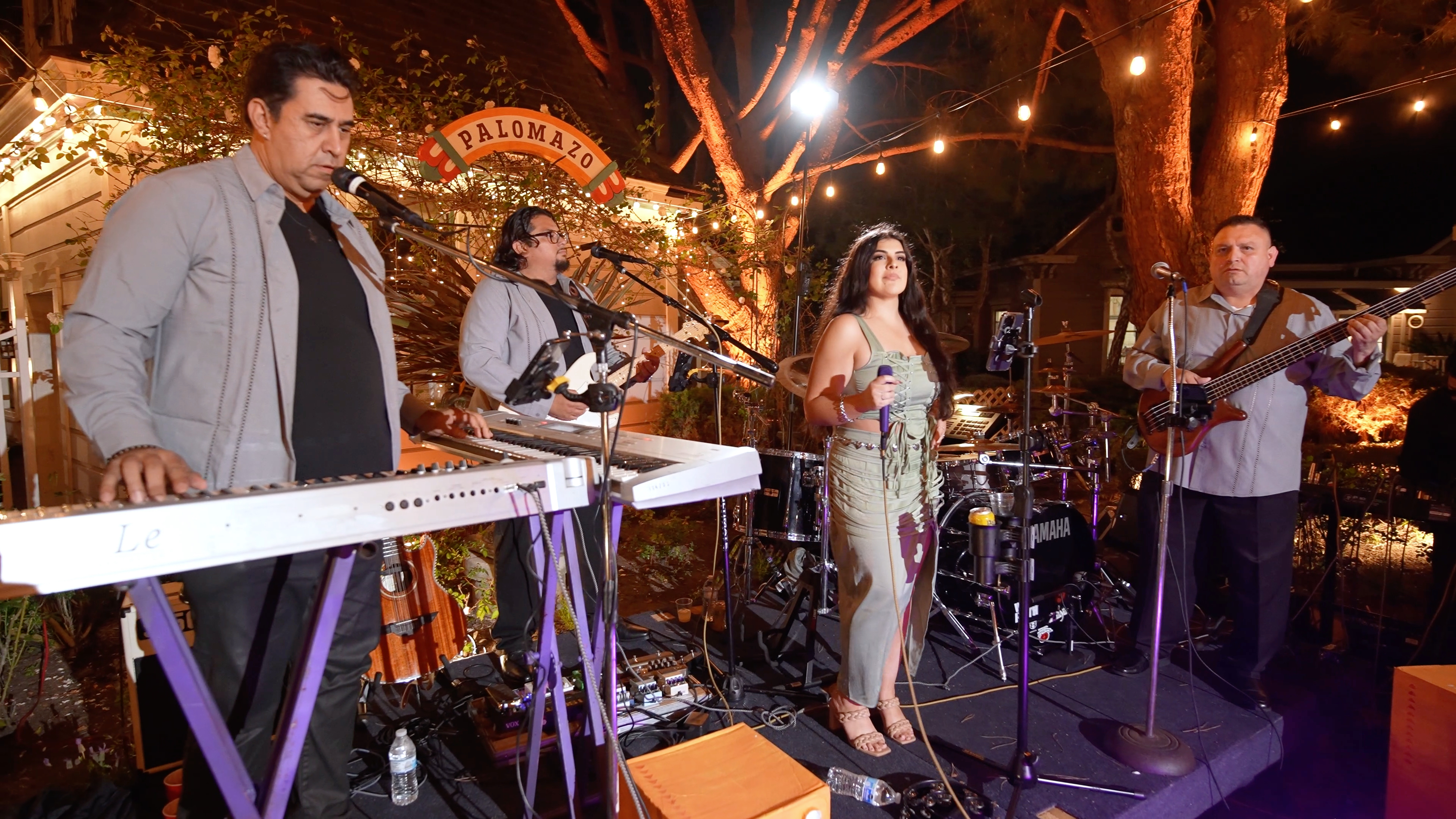 Grupo Monitor performing live outdoors, with keyboardist, guitarist, and vocalist